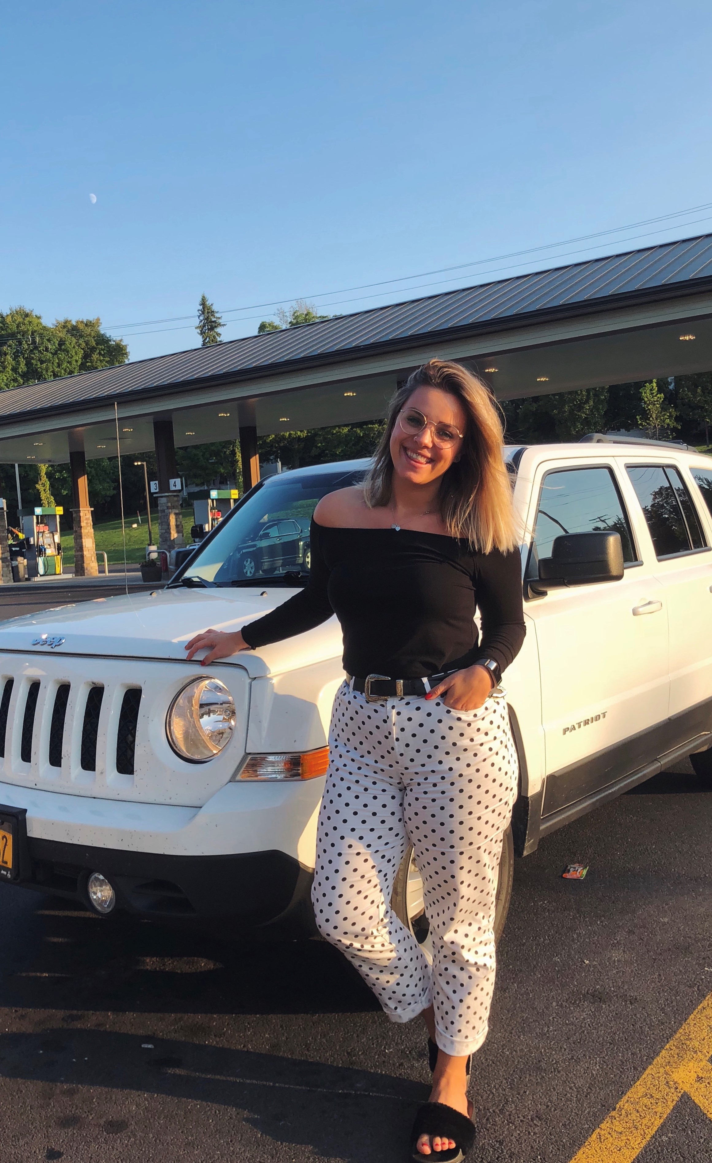 Woman wearing closet staples in front of her car.