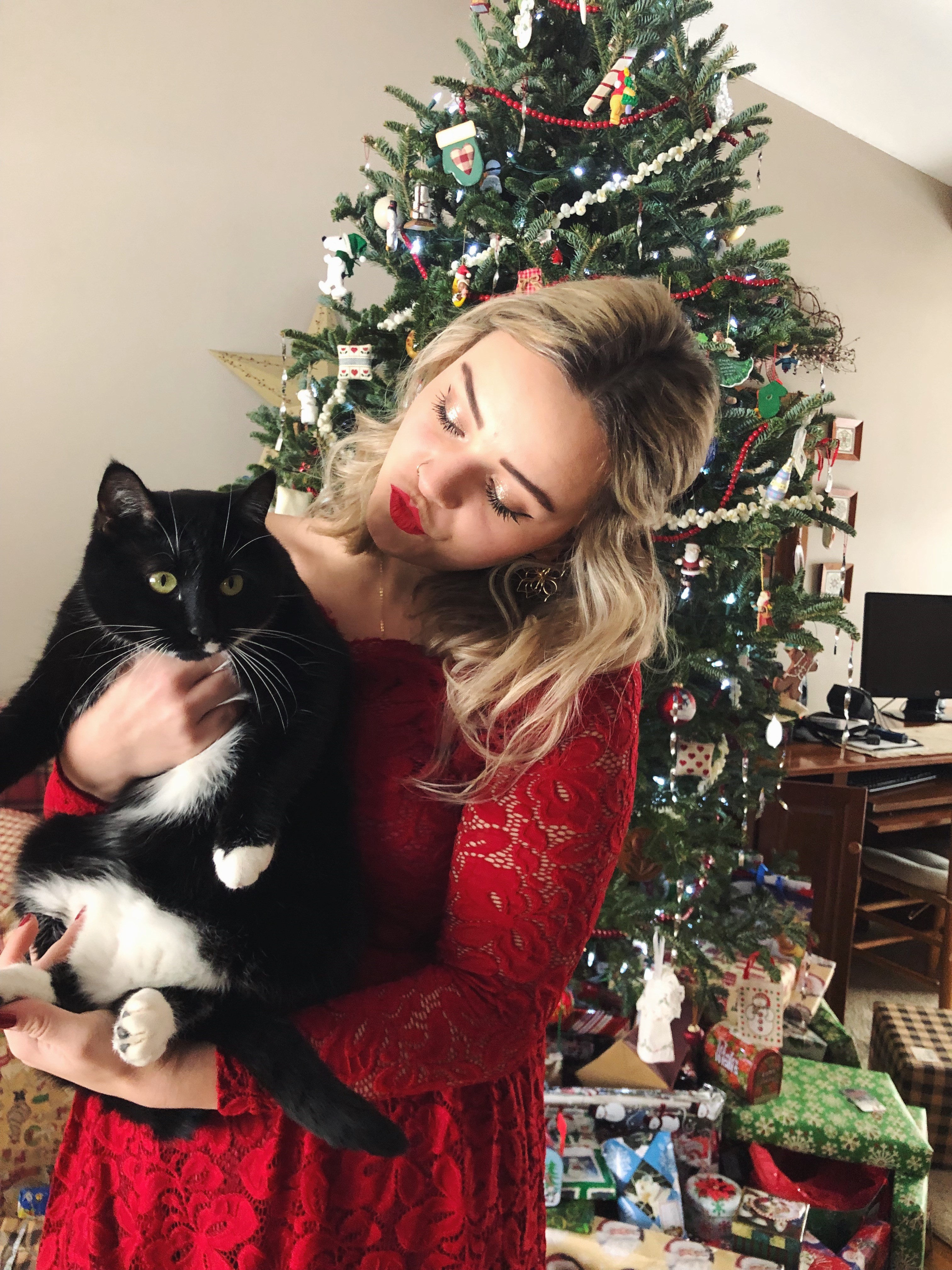 Woman wearing a red dress with a black cat in front of a Christmas tree.