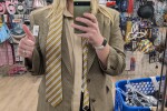 Woman wearing a tan button up shirt, brown blazer, and brown striped tie, giving a thumbs up