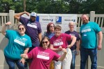 Larger group of people posing in front of a Goodwill branded backdrop wearing 988 T shirts
