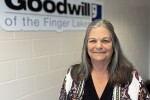 Woman with long salt and pepper hair posing in front of a Goodwill sign
